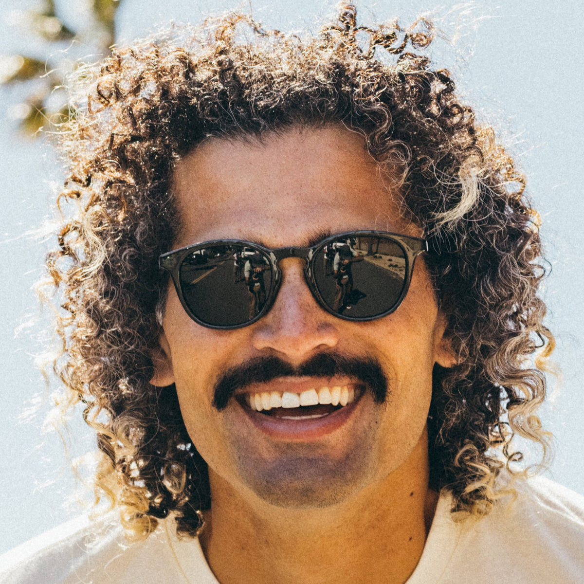 Man with curly hair wearing sunglasses against a light background