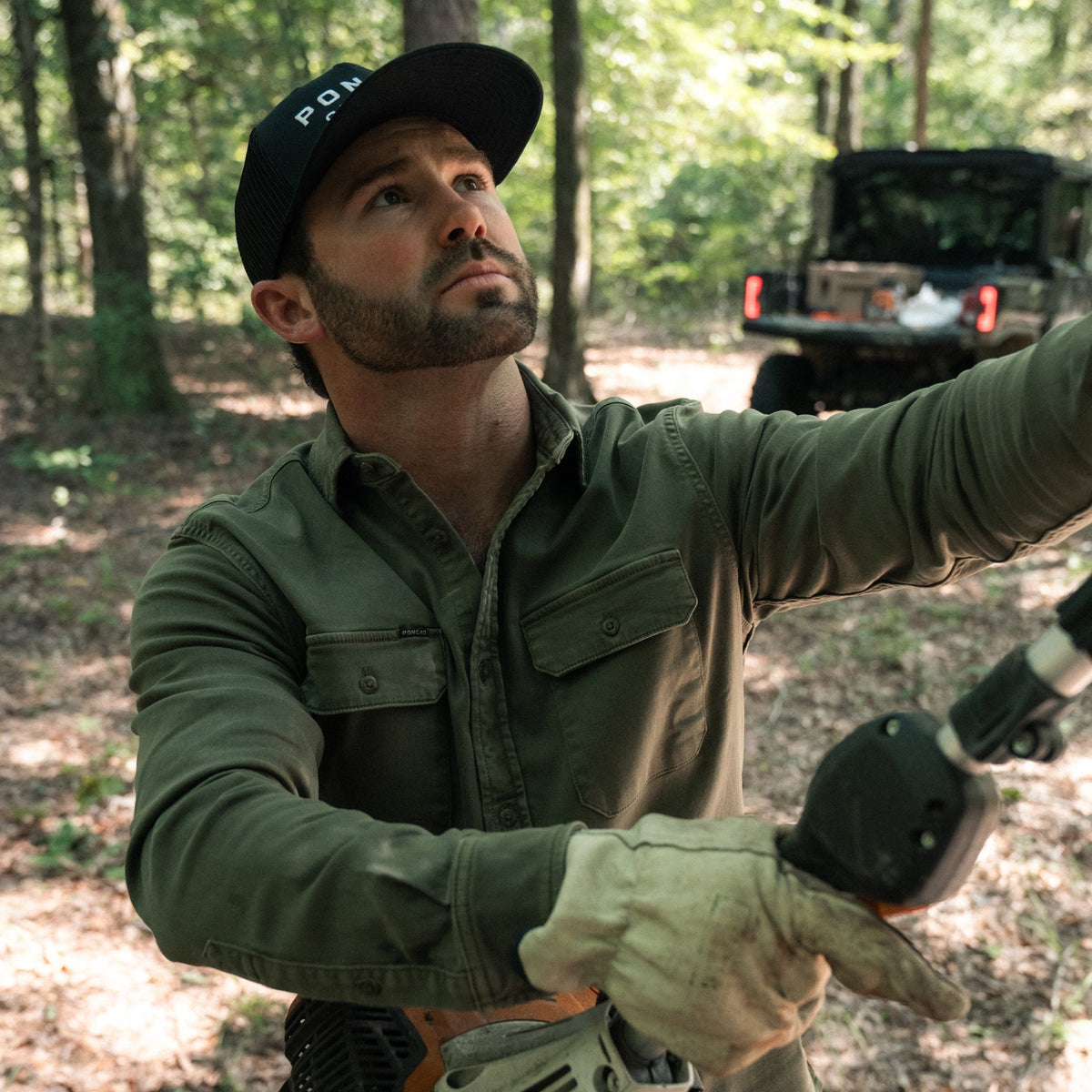 The Buck Snort green outdoor shirt worn by a man exploring a wooded trail beside an off road vehicle