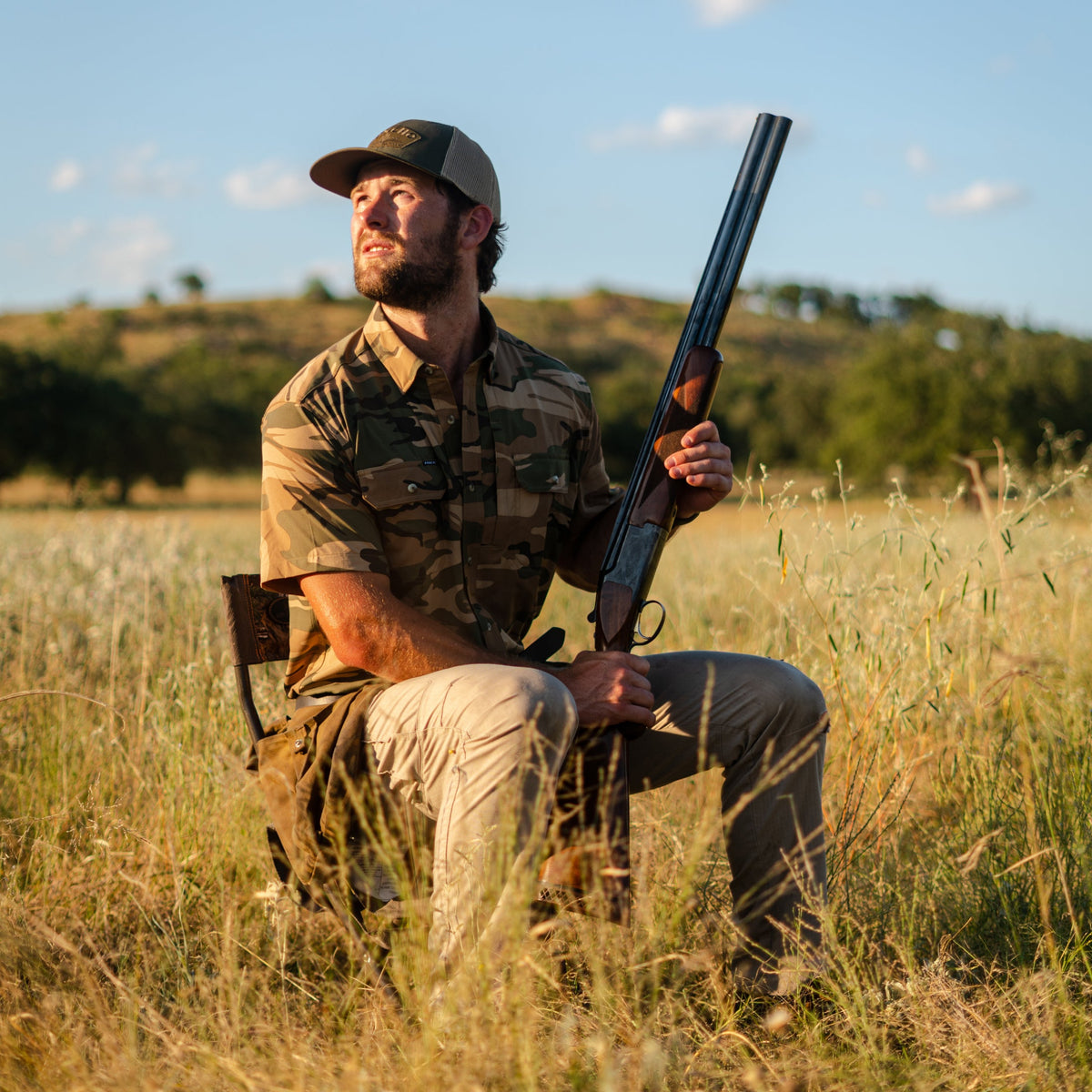 Man wearing The Cordoba shirt sitting in field holding shotgun