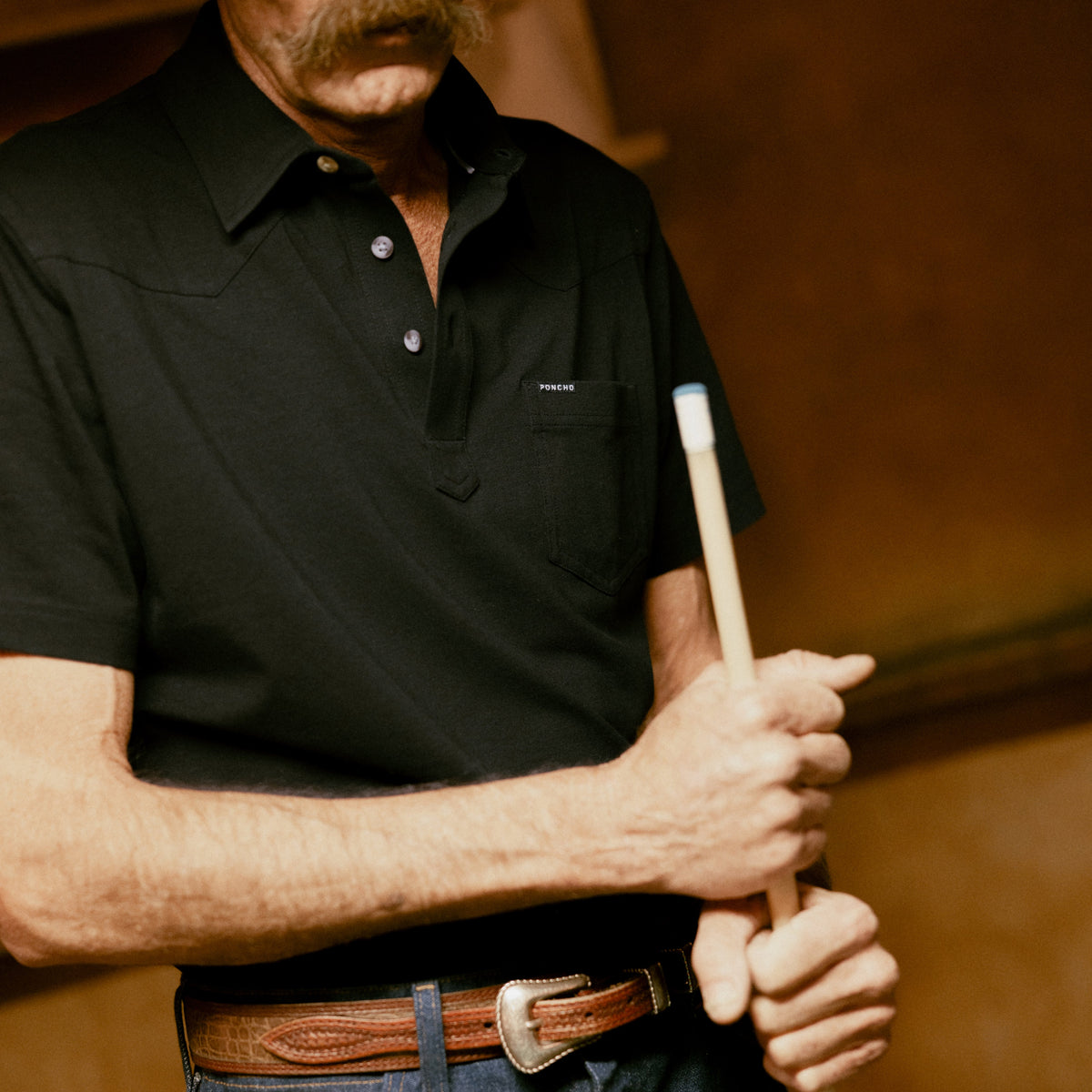 Man wearing The Permian black shirt holding a pool cue indoors
