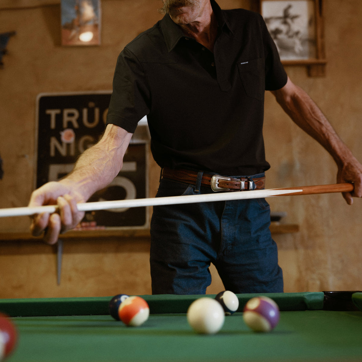 Man wearing The Permian black shirt playing pool indoors