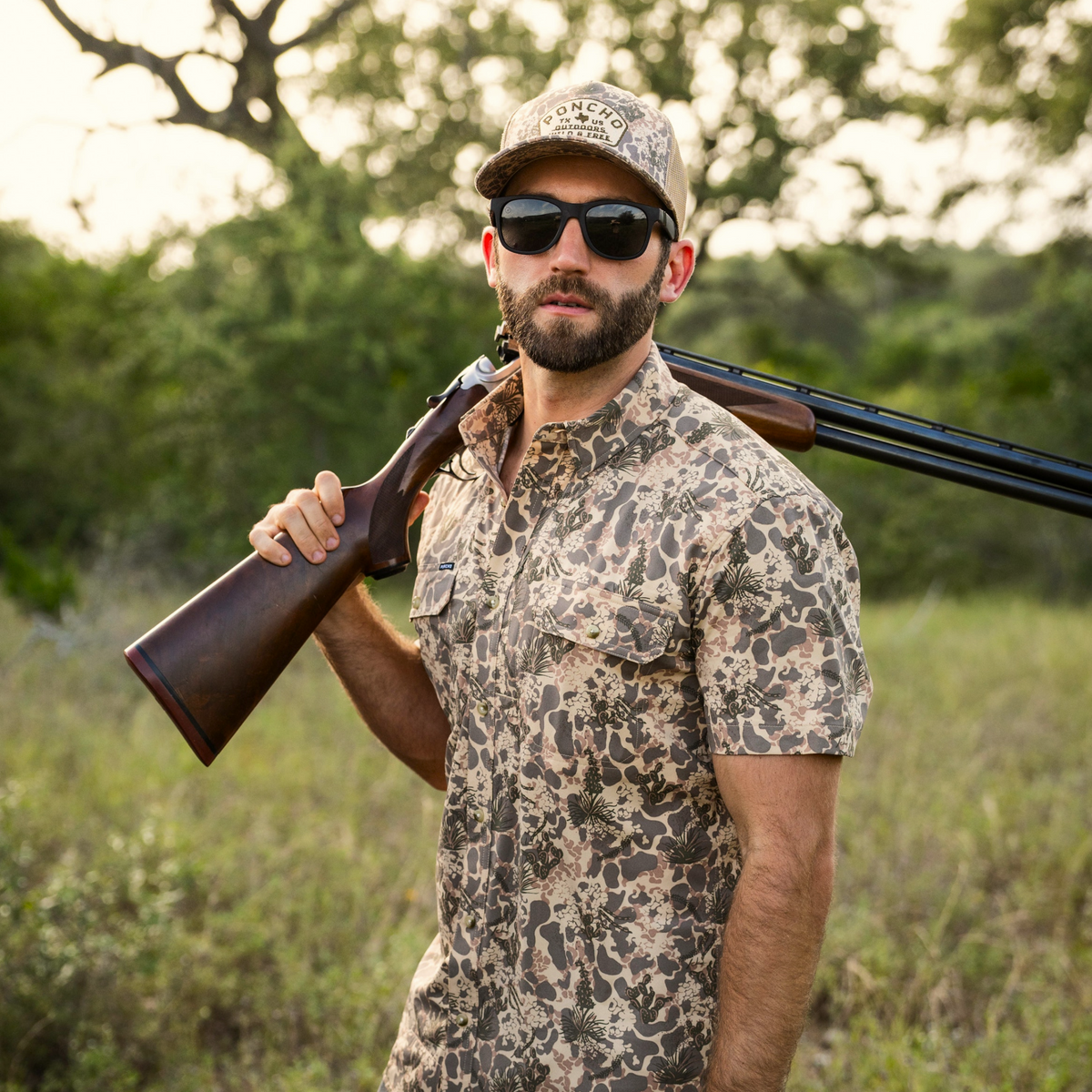 Man wearing The Albany shirt with a camouflage pattern, outdoors holding a shotgun over his shoulder and wearing sunglasses and a matching cap.