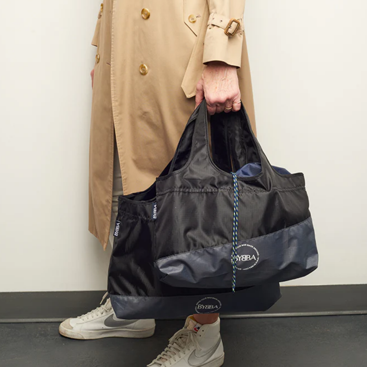 Packable, foldable, reusable tote bag made from recycled ocean plastic by BYBBA, held by person in trench coat.