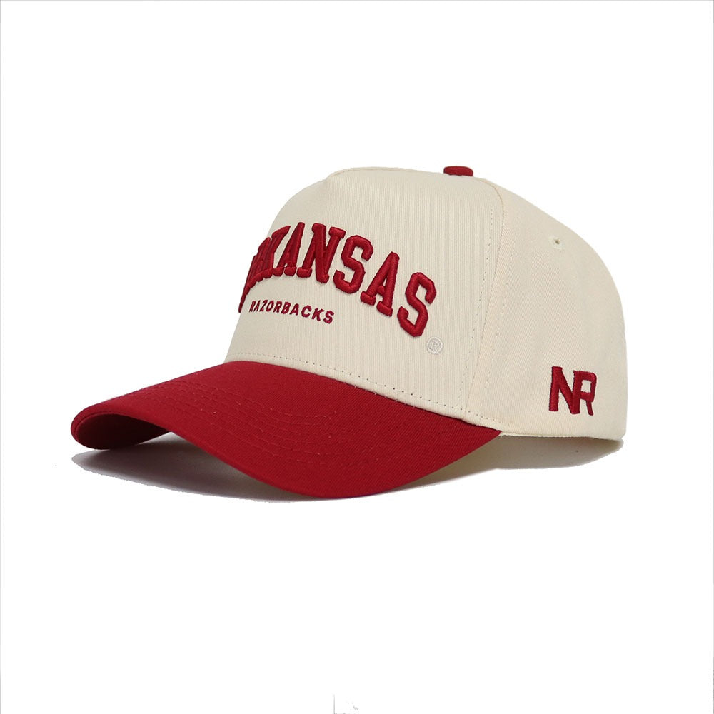 The Arkansas Razorback Hat by No Rivals features a cream and red design with ARKANSAS RAZORBACKS on the front, NR on the side, a red bill and button. Officially licensed for an authentic gameday look.