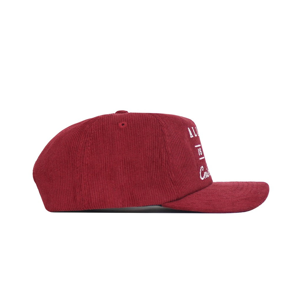 A side view of the No Rivals Alabama Vintage Cord Hat in red corduroy with white embroidered front text, featuring an unstructured fit, displayed against a plain white background.