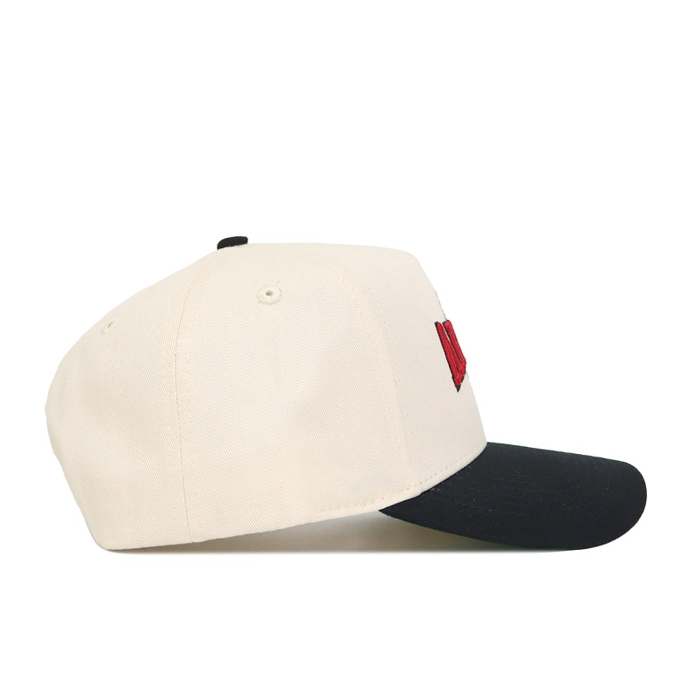 The Arizona Ballpark Hat by No Rivals is a cream-colored, structured snapback with a black brim. Made from high-quality cotton, it features a red embroidered design partially visible on the side front panel.