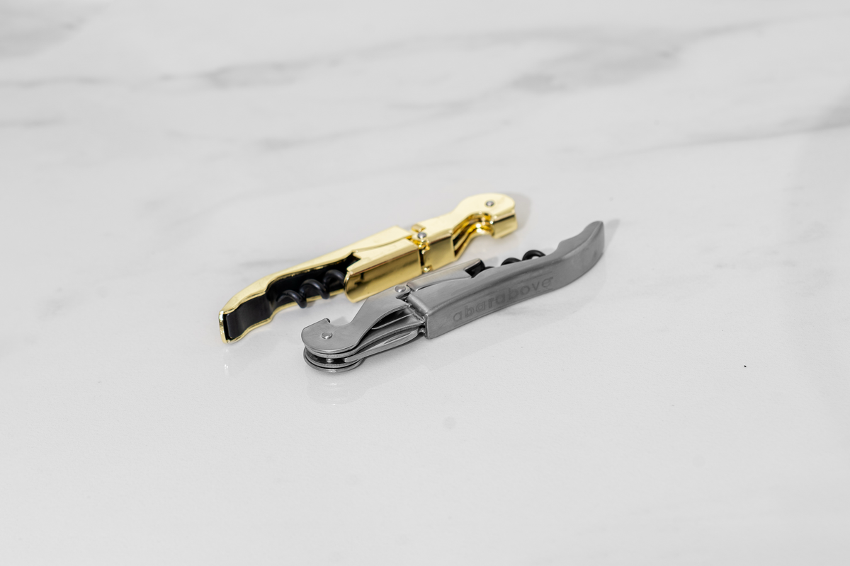 A gold and a matte silver professional wine opener resting on a white marble surface.
