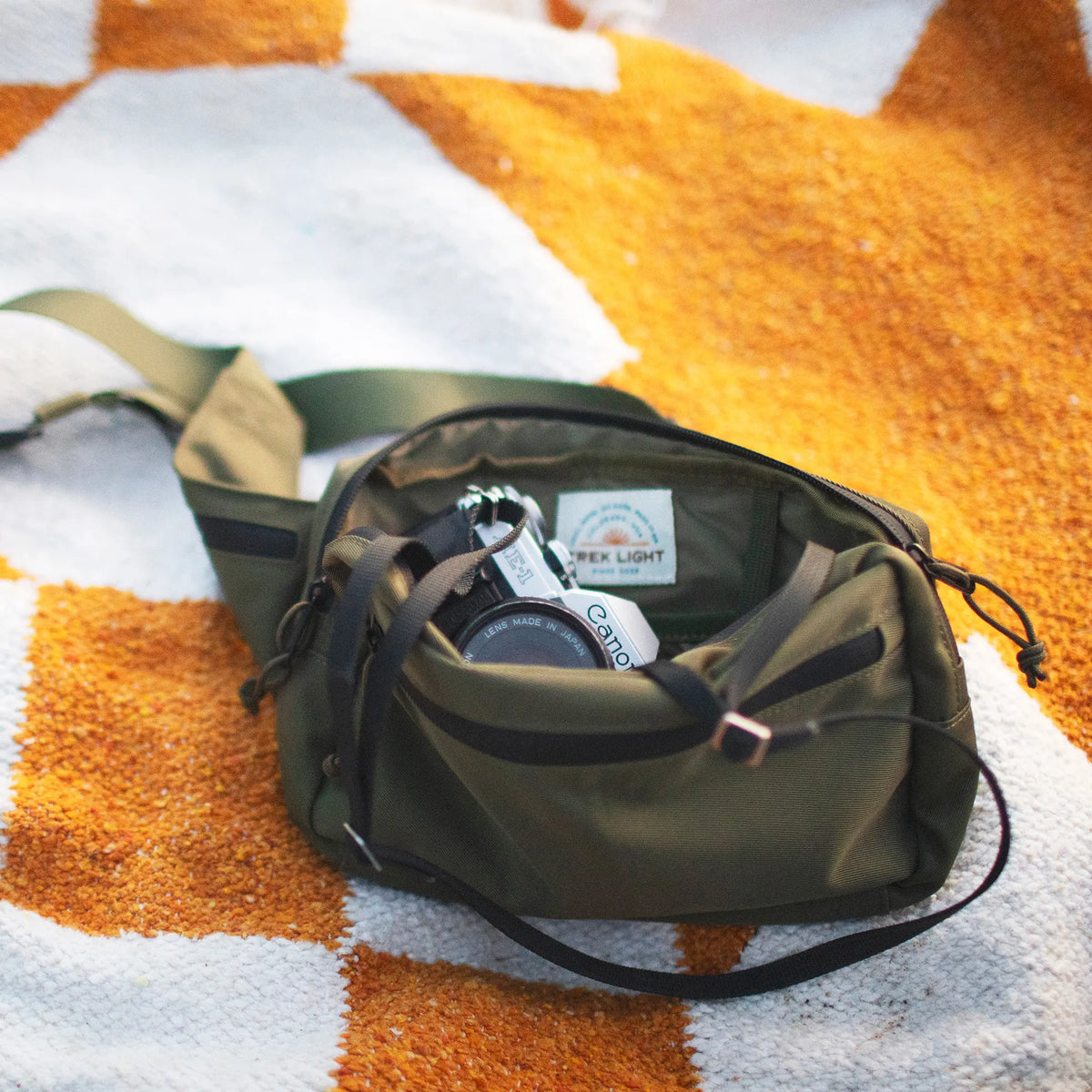 Everyday Fanny Pack (Fern) on a picnic blanket, showcasing its spacious and versatile design with multiple pockets and zippers.
