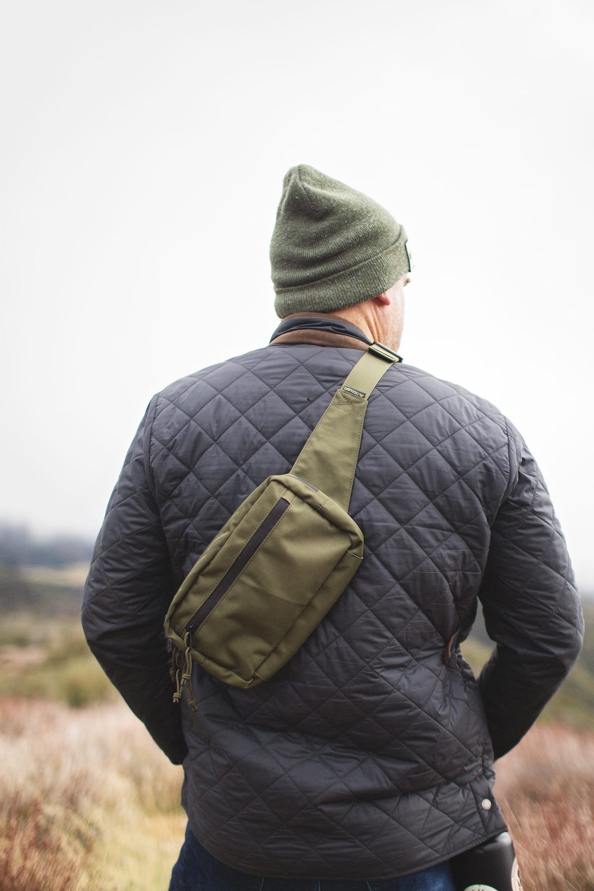 Man wearing Everyday Fanny Pack (Fern) as a crossbody sling, showcasing its versatility in outdoor setting.