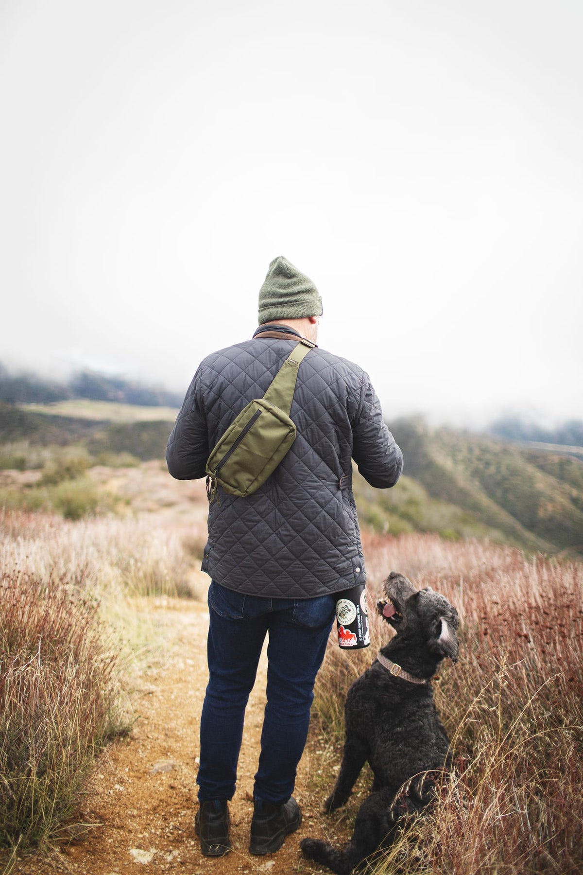 Person hiking with dog wearing Everyday Fanny Pack (Fern) as a crossbody sling, highlighting outdoor versatility and style.
