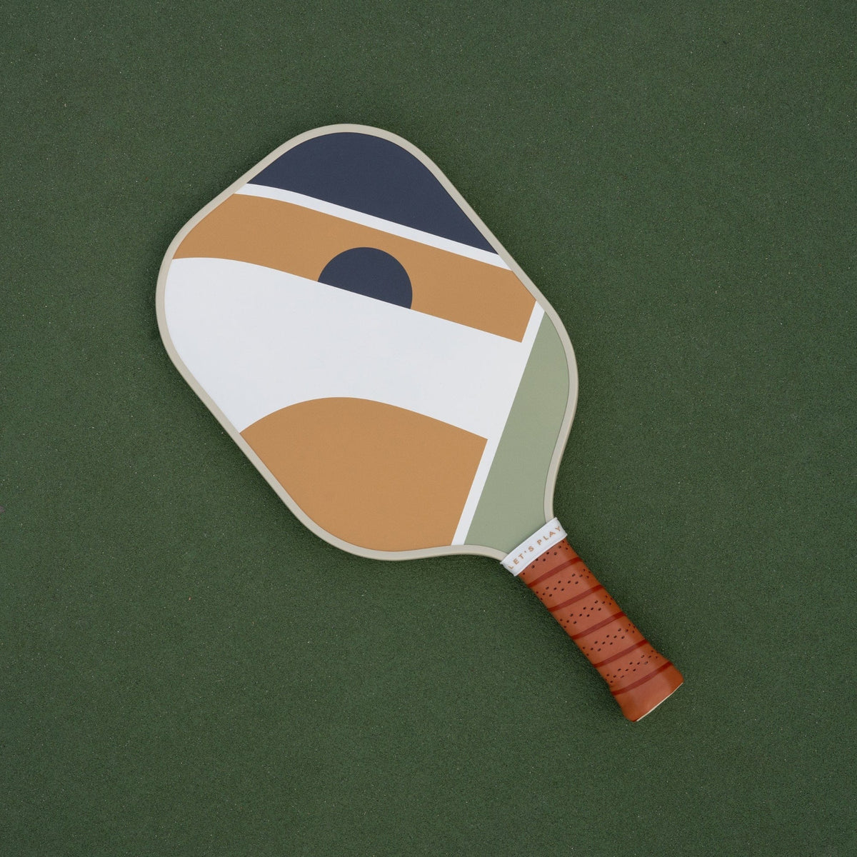 Recess Sonny pickleball paddle with colorful geometric design lying on green pickleball court