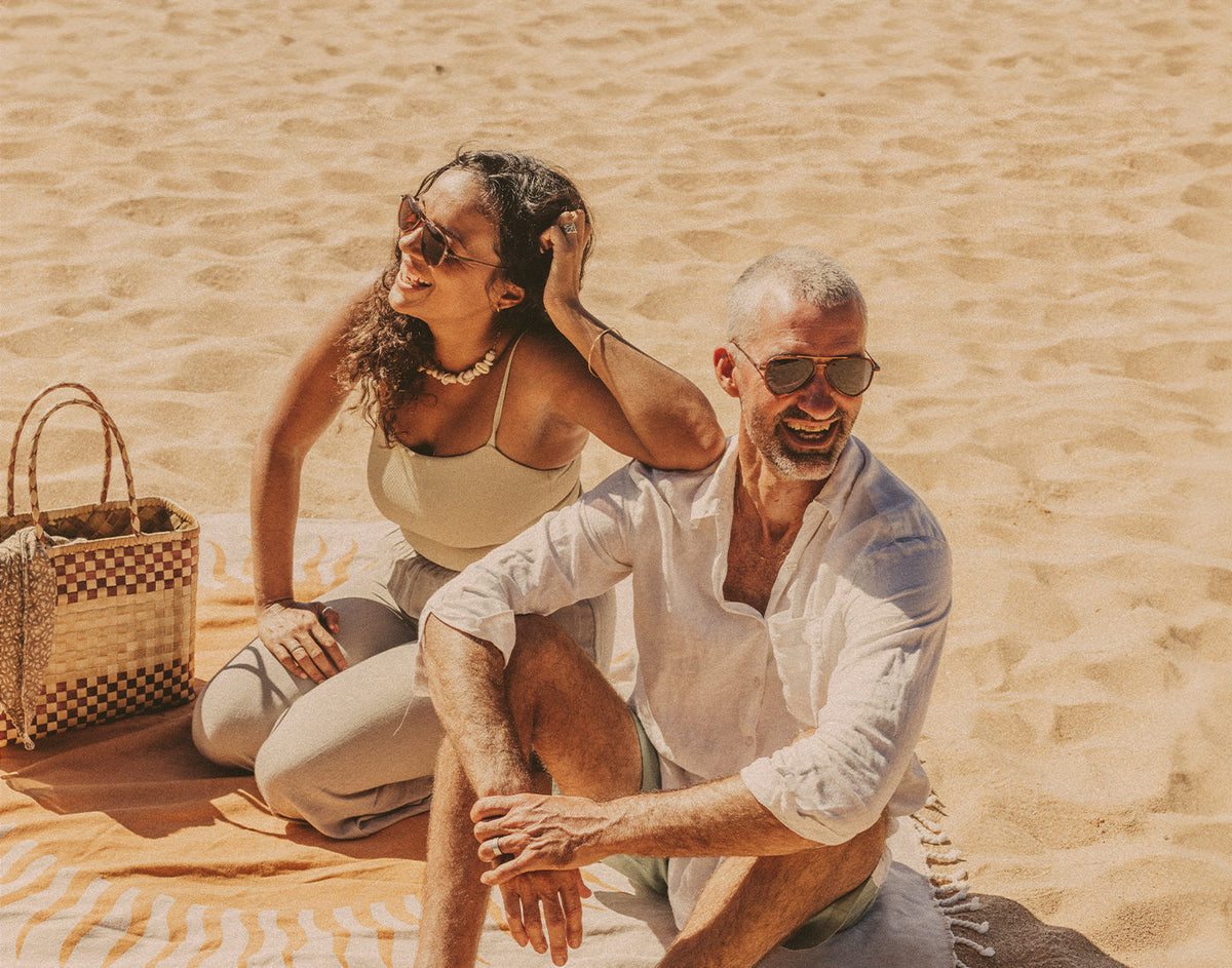 STORY man and woman sitting on the beach wearing sunski astra sunglasses