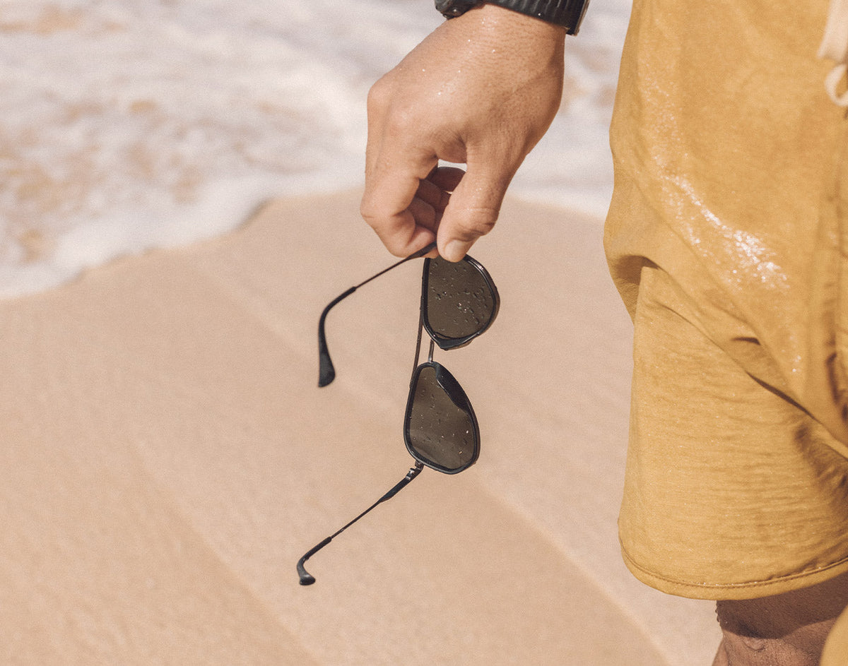 STORY hand holding sunski astra sunglasses on the beach