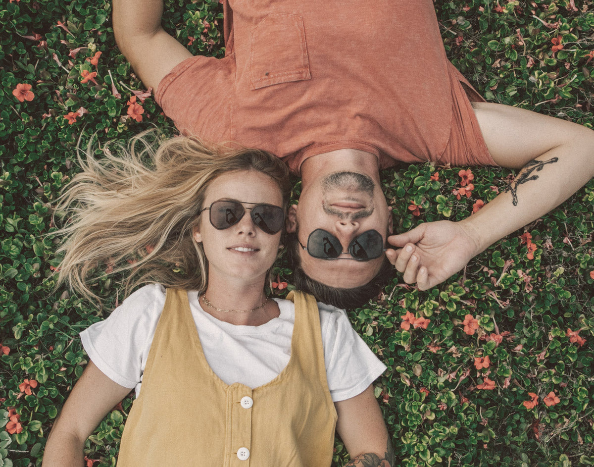 STORY guy and girl laying in the grass wearing sunski astra sunglasses