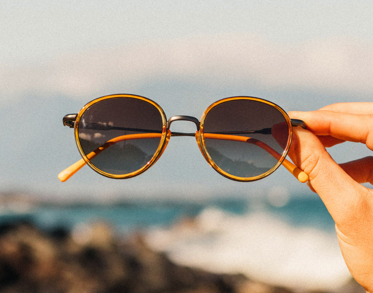 STORY hand holding sunski baia sunglasses by the beach