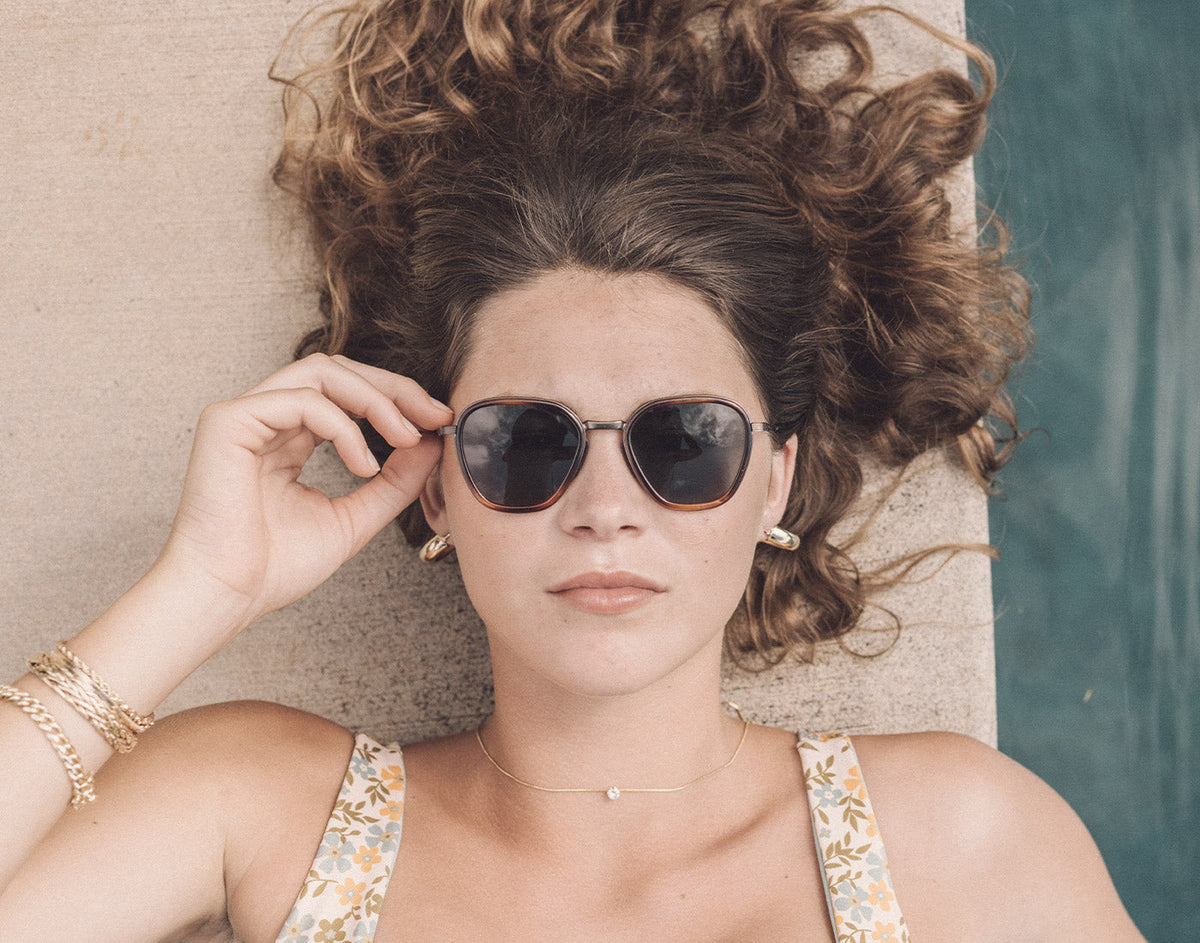 STORY girl laying by pool looking straight wearing sunski bernina sunglasses