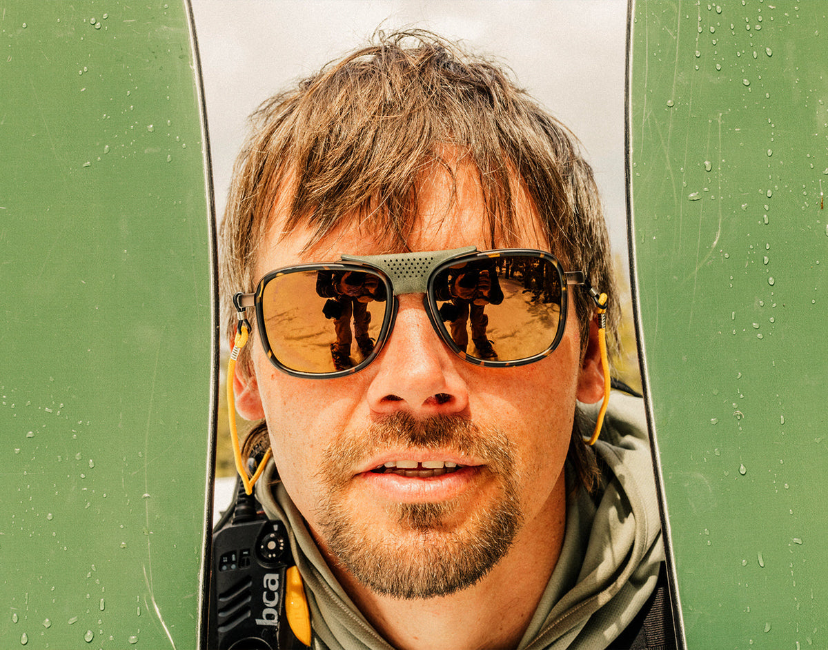 STORY guy holding skis next to his face wearing sunski ferrata sunglasses