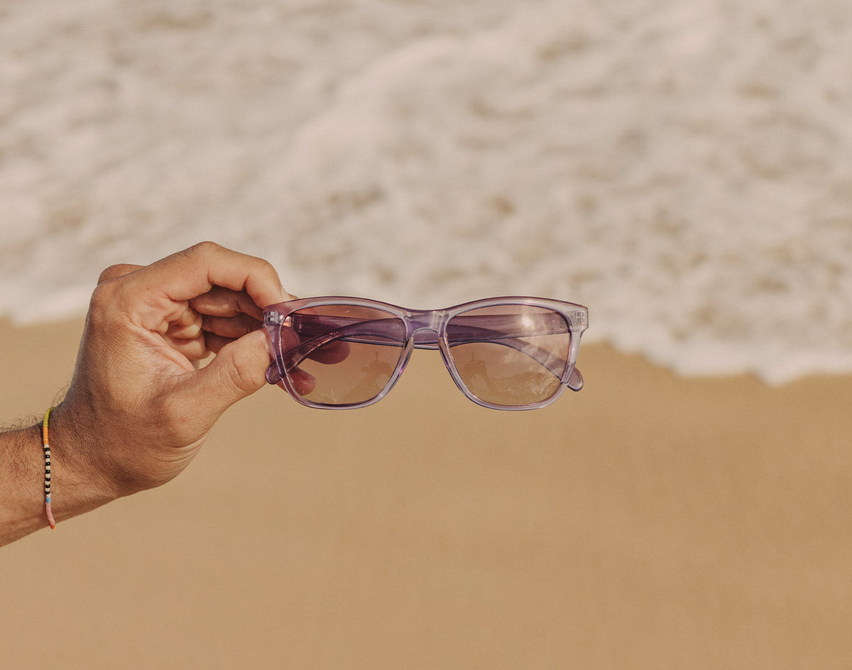 STORY hand holding sunski headland sunglasses on the sand