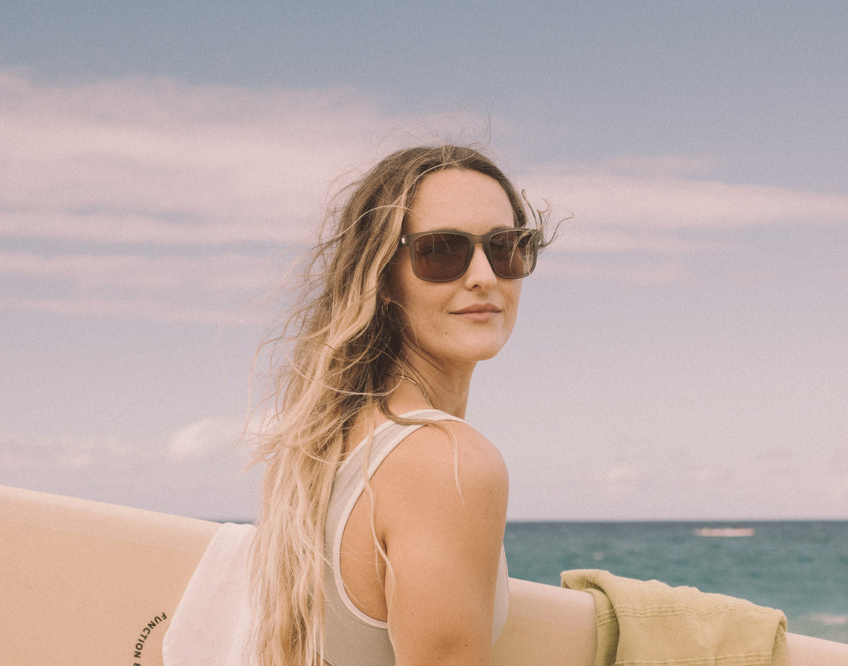 STORY girl holding surfboard wearing sunski kiva sunglasses