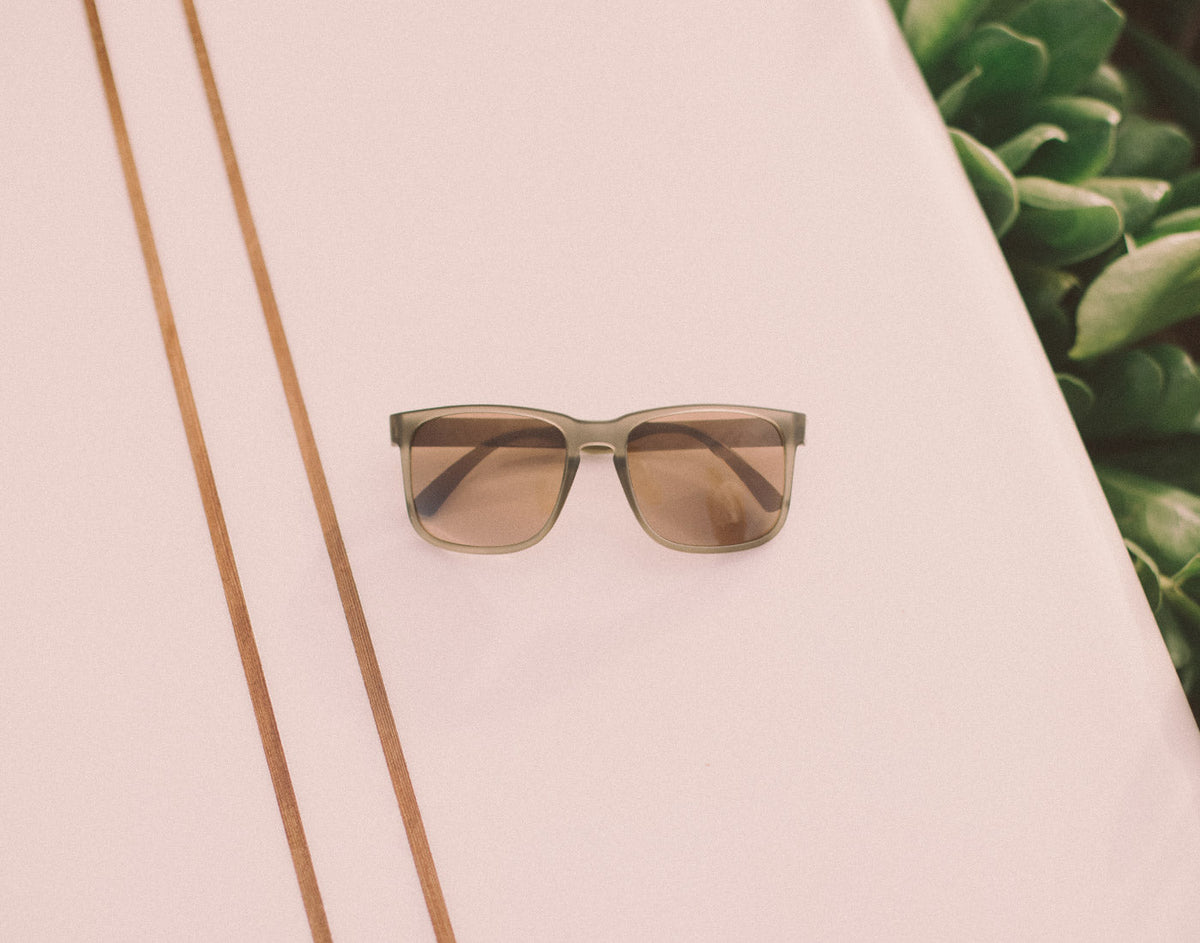 STORY sunski kiva sunglasses laying on a surfboard