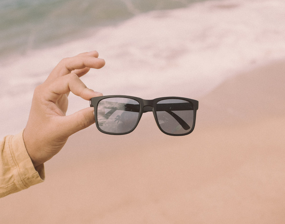 STORY hand holding sunski kiva sunglasses on the beach