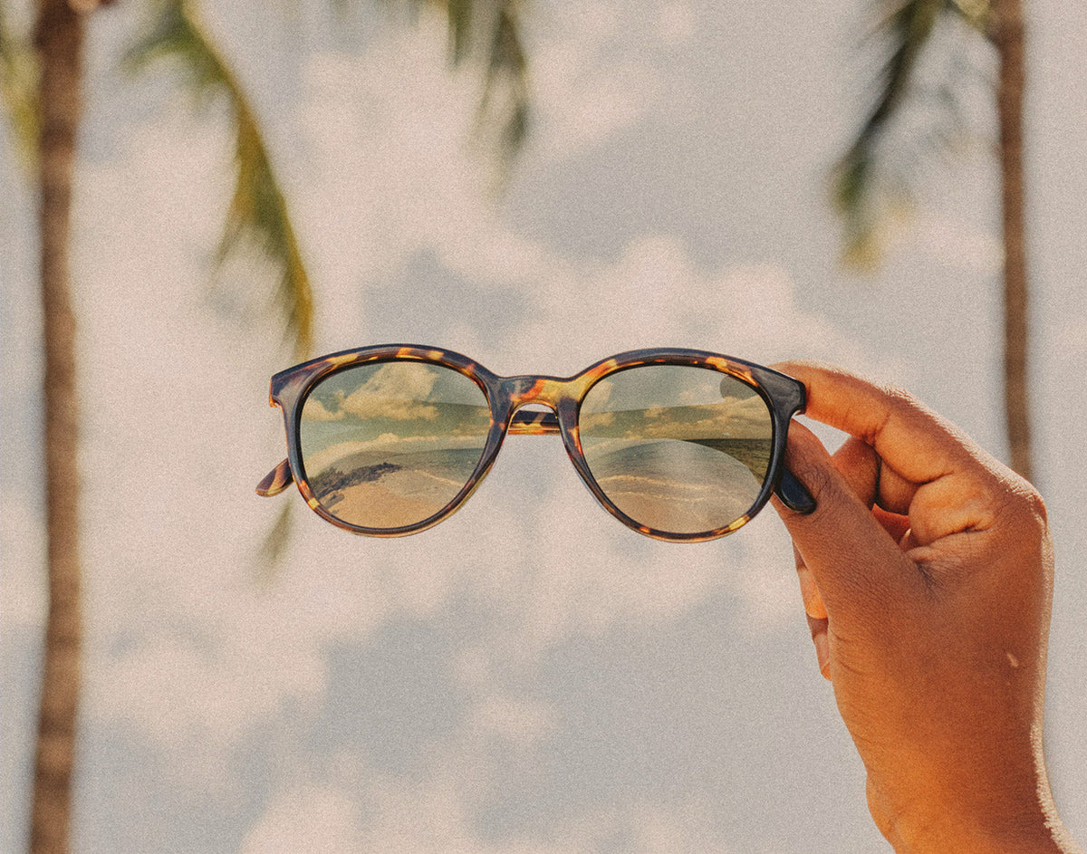STORY hand holding sunski makani flash gold sunglasses in the sky