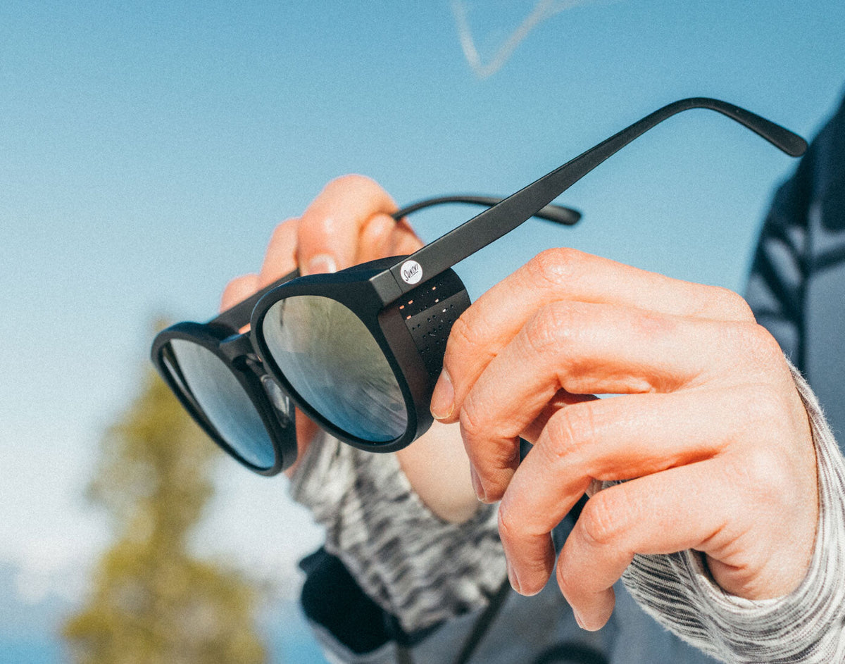 STORY Person holding a pair of black sunglasses with a blurred outdoor background