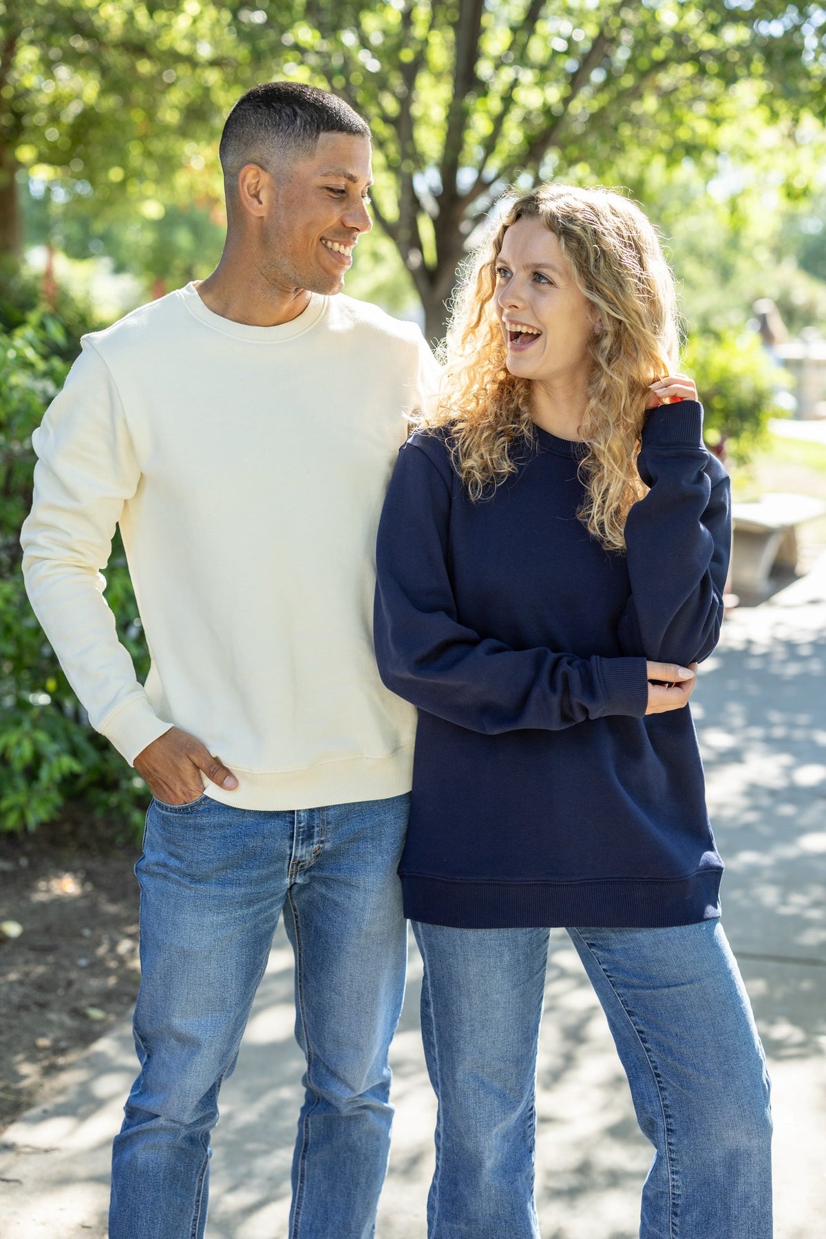 Two people standing outdoors, one wearing a white sweatshirt, the other in a navy sweatshirt